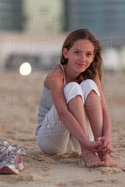 Teen Girl in Beach Clothes and Hat is Sitting on Lounger on the Seashore. Charming Teen Girl in Beach Clothes and Hat is Sitting on Lounger on the Seashore. She is smiling and …
